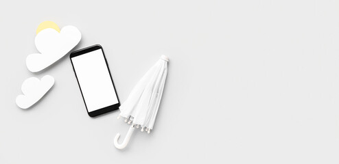 Mobile phone with blank screen, small umbrella and paper clouds on light background. Weather forecast concept