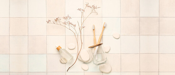 Holder with bamboo tooth brushes, bottle of serum and spa stones on light tile background
