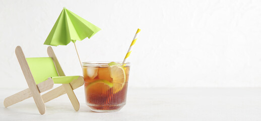 Glass of cold Cuba Libre cocktail, small deck chair and umbrella on white background with space for text