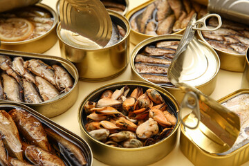 Many opened tin cans with different fish on beige background
