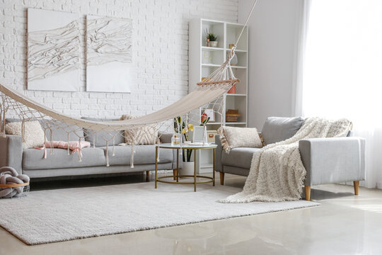 Interior of light living room with hammock and grey sofas