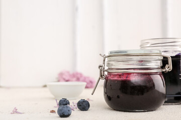 Jar of sweet blueberry jam and berries on white table, closeup