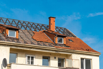 Parts of the roof of an apartment building with dismantled tiles under the blue sky.