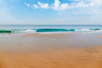 Fototapeta na wymiar Ocean waves on the sandy beach coast under the beautiful blue sky with clouds of Sri Lanka island.