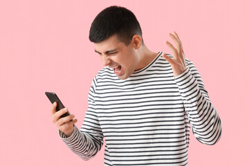 Aggressive young man with smartphone on pink background