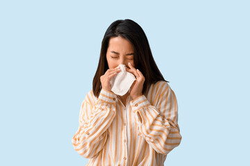 Allergic Asian woman sneezing on blue background