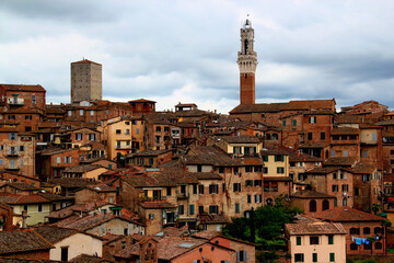Fototapeta na wymiar Photo of the historic part of the city with the tower of Torre del Mangia in the center of the photo against a stormy sky in the city of Siena, Tuscany region, Italy