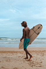 company of young guys Sri Lankans, Indians surfers on the ocean coast with a surfboard, sporty...