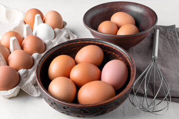 Brown chicken eggs in a cardboard packing container, and in a bowl on a table with a whisk to beat the eggs.