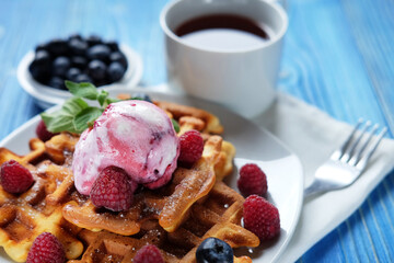 Waffles with ice cream and raspberries for breakfast over blue wooden table.