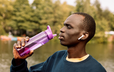 Young handsome African American sport man tired and thirsty after running workout holding bottle...