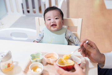 パパに離乳食を食べさせてもらってご機嫌笑顔の生後8か月の赤ちゃん