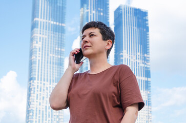 smiling woman talking on smartphone in background of high-rise building with a blue glass facade.