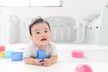 自然光が入るリビングのプレイマットで知育おもちゃを使って遊ぶご機嫌笑顔な生後8か月の赤ちゃん