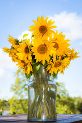 bunch of yellow sunflowers in a glass vase against blue sky