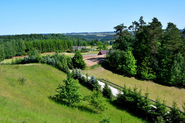 A view from a tall hill covered with trees, forests, moors, fields, and other flora with the view of a vast round and clean lake or river in the distance seen on a sunny summer day in Poland