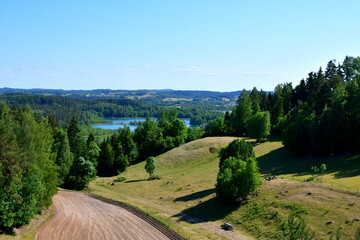 A view from a tall hill covered with trees, forests, moors, fields, and other flora with the view of a vast round and clean lake or river in the distance seen on a sunny summer day in Poland