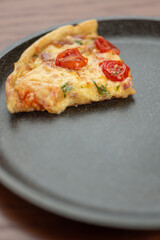 A piece of pizza on a dark frying pan.