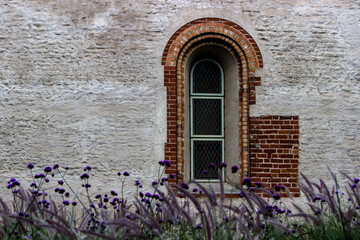 Old church wall with window and flowers in foreground.