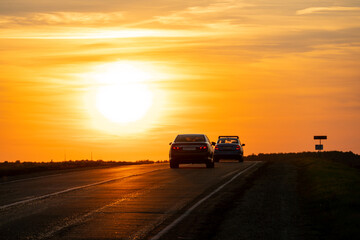 The silhouette of a car on the road against the background of the sun. The car is driving on the highway during sunset. The concept of travel and freedom.