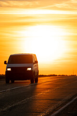 The silhouette of a car on the road against the background of the sun. The car is driving on the highway during sunset. The concept of travel and freedom.