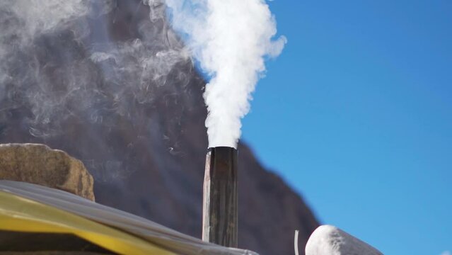 Slow motion shot of smoke being emitted from the Chimney of home in the mountains at Zanskar in Ladakh, India. Smoke being emitted from inside the home due to burning of firewood to keep warm in cold.