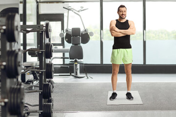 Fototapeta na wymiar Full length portrait of a young man in sportswear posing in a gym