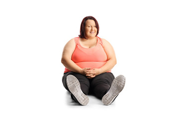 Overweight young woman in sportswear sitting on the ground