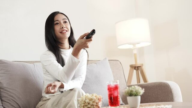 Asian young beautiful woman watching fun movie on television at home. Attractive casual girl feel happy and relax, sit on sofa having fun watch comedy video on TV in house. Activity lifestyles concept