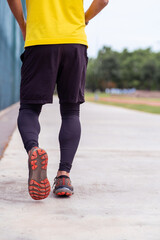 Man in leggings and shorts running along empty road on public urban sports ground in green park person practicing activities of healthy lifestyle close backside view
