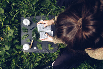 girl holding a deck of cards above the fortune telling table on a grass, where there are tarot...