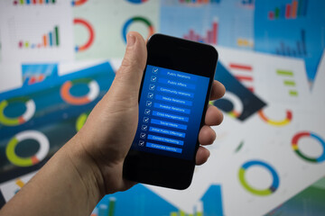 Ręka trzymająca telefon z niebieskim ekranem na tle wykresów.