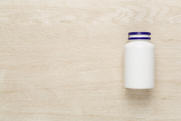 Plastic bottle with vitamins on wooden background, top view