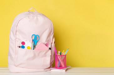 Pink school backpack with stationery on wooden table