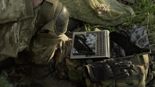 Soldier uses a tablet computer with a keyboard and a phone for reconnaissance. Computer technology in the modern army. Soldier touches the tablet screen with his hand.