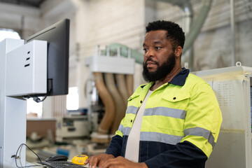 Black man engineer using tablet computer operating CNC machine for cutting wood in furniture factory. Male technical maintenance and programing to machine for making wooden product.