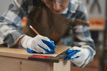 Female carpenter hands wear gloves using square ruler tool measuring length of wooden plank in...