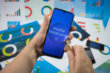 Media relations. Telefon z niebieskim ekranem trzymany w rękach. Napis na ekranie jest powiększony przez lupę. - obrazy, fototapety, plakaty