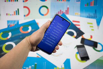 Ręka trzymająca telefon z niebieskim ekranem z napisami na tle wykresów.