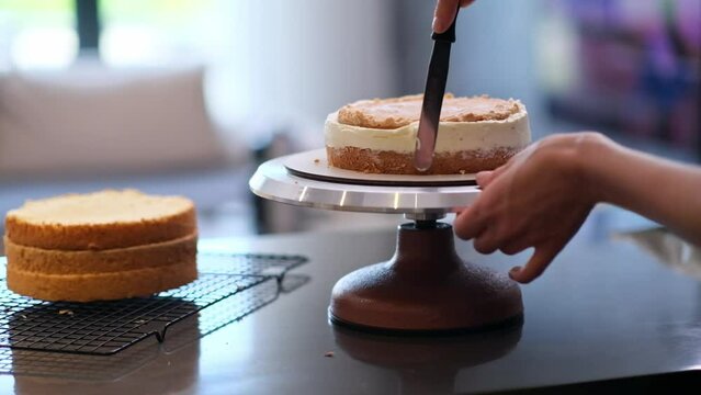 Skilled self-made confectioner smearing white cream around cake layer made of lactose free products woman standing at kitchen table using professional utensils to make handmade pastry closeup