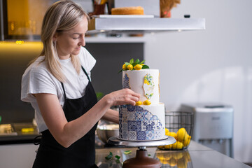 Focused blonde woman putting confit yellow lemons on large wedding cake standing at table in modern...