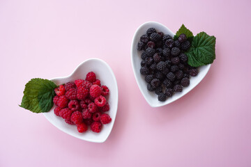 Ripe raspberries and blackberries lie in white plates in the form of hearts