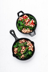 Vegan dinner, beans with tomatoes and kale in cast iron skillet, top view