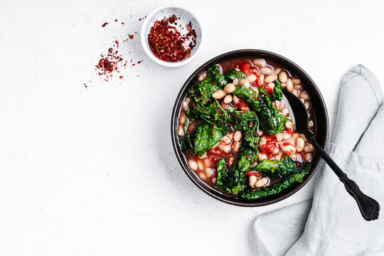 Vegan dinner, beans with tomatoes and kale in ceramic bowl, top view