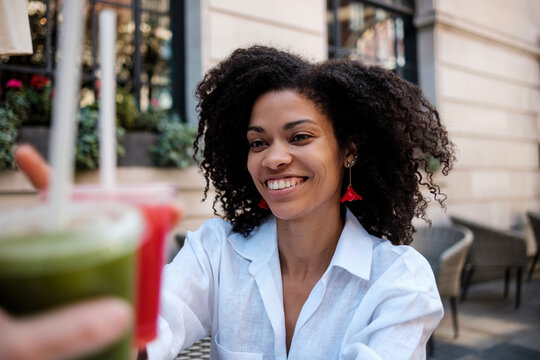 Smiling curly woman toasting with juice in a terrace.