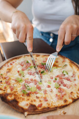 Process of woman slice thin pizza in cafe. Woman use fork and knife. Pizza with bacon and onion