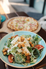Delicious food on table in cafe. Caesar salad and thin pizza with bacon