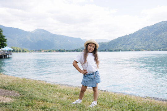 Adorable little girl in denim skirt white t-shirt and Panama straw stand in front of big beautiful lake