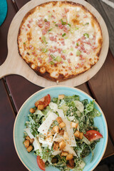 Top view of delicious food on table in cafe. Caesar salad and thin pizza with bacon