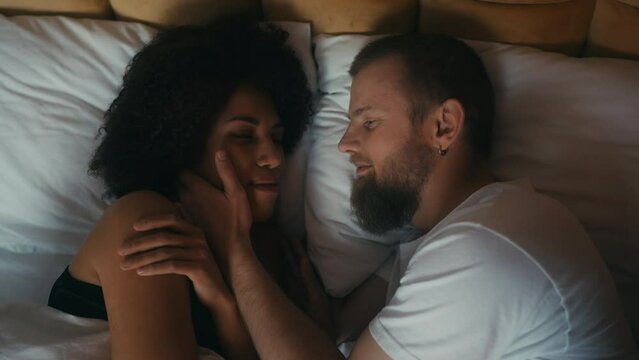 Interracial couple lying embraced in bed, love and tenderness, happy marriage